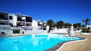 A swimming pool with a curved edge, surrounded by a pebble walkway. There are lounge chairs and a lifebuoy near the pool.