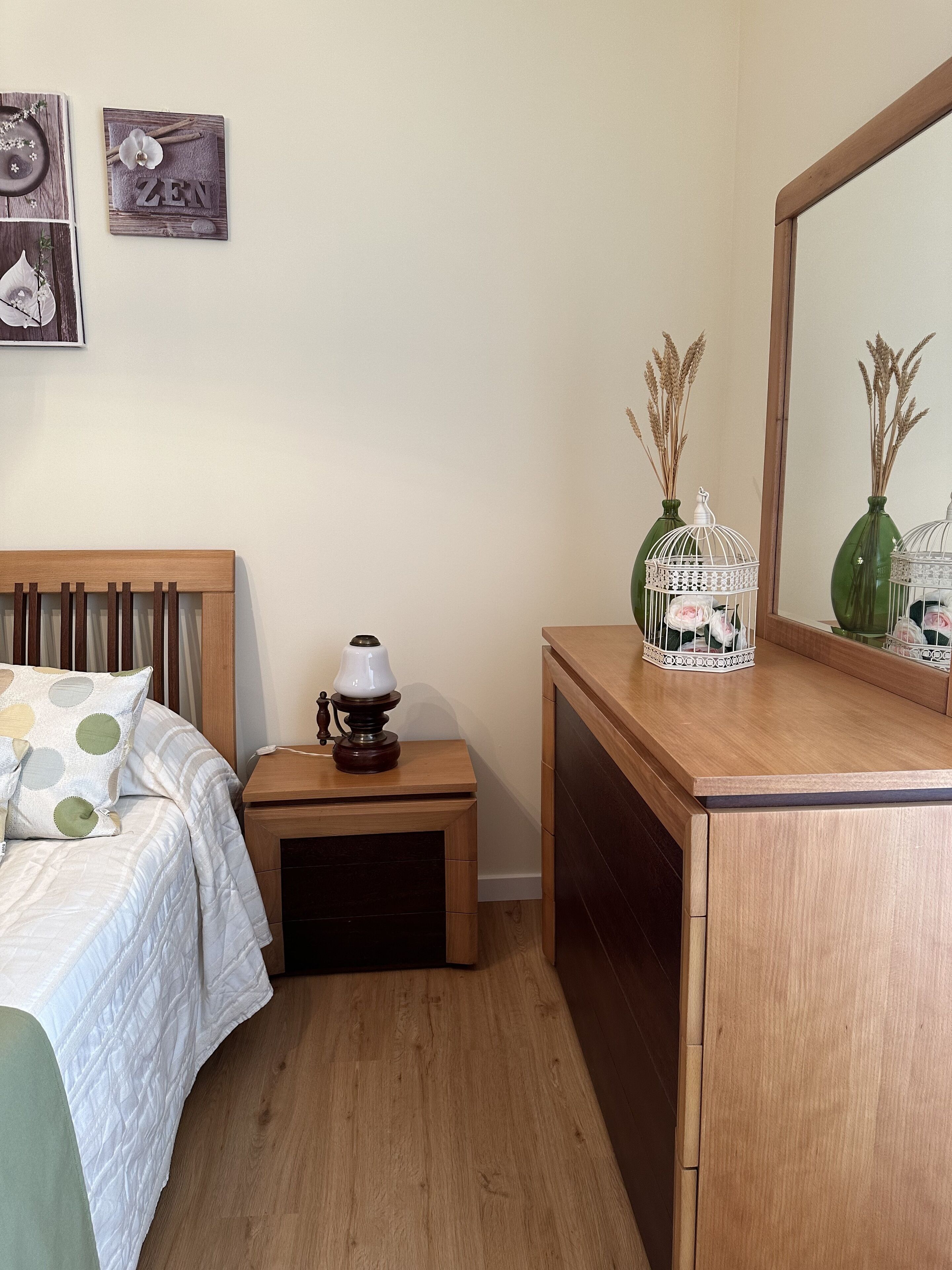 A neatly arranged bedroom with a bed, bedside table, dresser, and wall decorations.