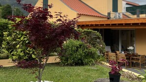 Una casa con fachada amarilla, tejado rojo y un pequeño jardín con un árbol y una planta en maceta.