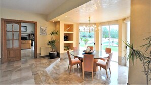 A spacious dining area with a round glass table, surrounded by chairs, and a view of the outdoors through large windows. - Country house with private pool & Tennis Court  - GREAT for families - Free Wifi (Bunyola)