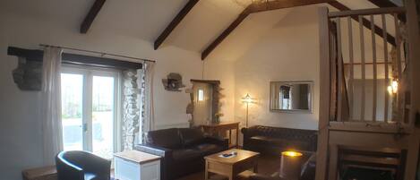 A cozy living room with a high ceiling, wooden beams, a stone wall, a fireplace, and a billiards table.