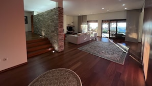 A spacious living area with a stone pillar, a white sofa, and a large window offering a view. - Luxury villa with pool and sea view -Free Wifi (povoa de varzim)