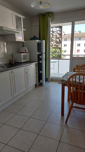 Una cocina con armarios blancos, microondas, tostadora y una mesa de comedor con sillas.
