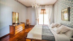Ein Schlafzimmer mit einem Holzbett, einem Schminktisch, einem Stuhl, einer Chandelier und einem fenster mit Vorhängen.
