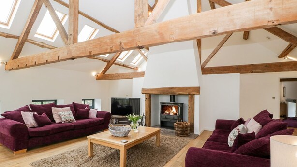 A spacious living room with high ceilings and exposed wooden beams, featuring two plush purple sofas, a wooden coffee table, and a fireplace. - Luxury Barn Conversion sleeps 11 in idyllic Herefordshire countryside (Hereford)
