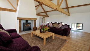 A spacious living room with a high ceiling, wooden beams, a fireplace, a sofa set, and a coffee table with flowers. - Luxury Barn Conversion sleeps 11 in idyllic Herefordshire countryside (Hereford)