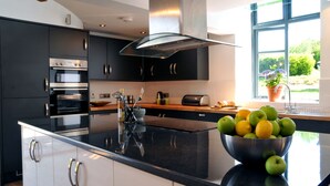 A modern kitchen with black cabinets, stainless steel appliances, and a large island with a bowl of fruit. - Luxury Barn Conversion sleeps 11 in idyllic Herefordshire countryside (Hereford)