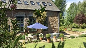 A stone house with a sloped roof, a patio with outdoor furniture, and a garden with various plants and flowers. - Luxury Barn Conversion sleeps 11 in idyllic Herefordshire countryside (Hereford)