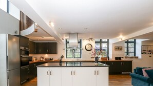 A modern kitchen with a central island, dark cabinets, stainless steel appliances, and a large window providing natural light. - Luxury Barn Conversion sleeps 11 in idyllic Herefordshire countryside (Hereford)