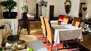 A dining area with a table set for four, surrounded by wooden chairs. There is a potted plant on a shelf to the left, and a mirror with a decorative frame on the wall to the right. - SUPERB LOFT APARTMENT, CLASS 4*, SOUTH-FACING WITH TERRACE IN THE ORANGERIE DISTRICT (Strasbourg)