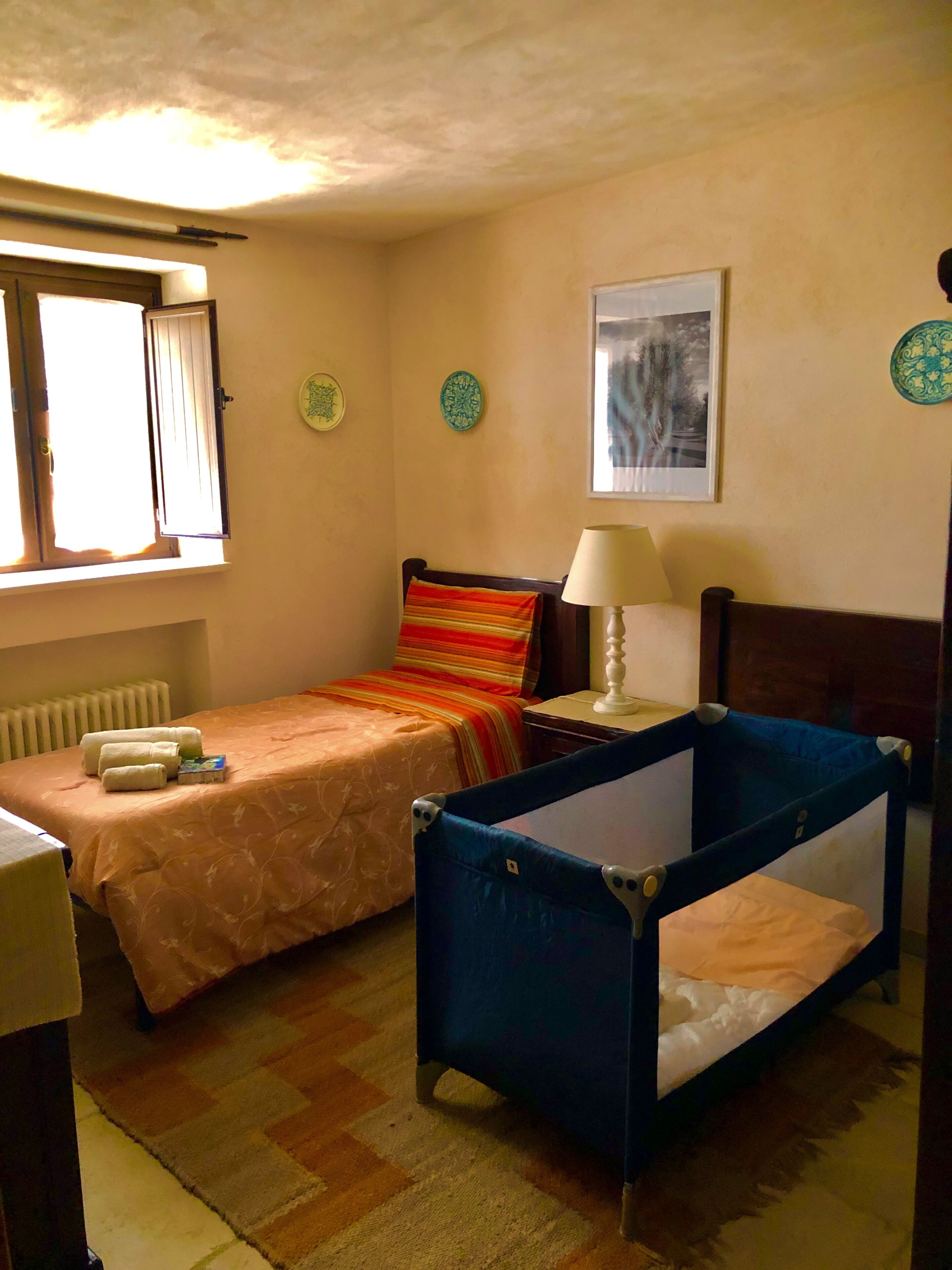 A bedroom with two beds, a window with curtains, a radiator, and a bedside table with a lamp.