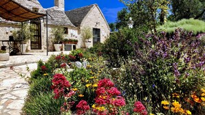 A stone building with a conical roof, surrounded by a garden with various flowers and plants. - Trullo With Private Pool (15x7), WI-FI free, tennis table,mountain bike for rent (Alberobello)