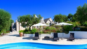 A pool area with lounge chairs and umbrellas, surrounded by stone walls and greenery. - Trullo With Private Pool (15x7), WI-FI free, tennis table,mountain bike for rent (Alberobello)
