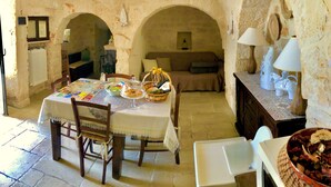A rustic dining area with a table set for a meal, a sofa, and a lamp on a wooden sideboard. - Trullo With Private Pool (15x7), WI-FI free, tennis table,mountain bike for rent (Alberobello)