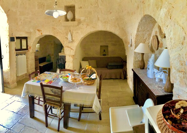 A rustic dining area with a table set for a meal, a sofa, and a lamp on a wooden sideboard. - Trullo With Private Pool (15x7), WI-FI free, tennis table,mountain bike for rent (Alberobello)