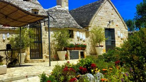 A stone building with a conical roof, a small tower, and a garden with colorful flowers. - Trullo With Private Pool (15x7), WI-FI free, tennis table,mountain bike for rent (Alberobello)