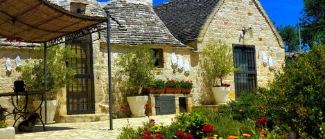 Un edificio in pietra con un tetto a cono, una piccola torre e un giardino con fiori colorati.