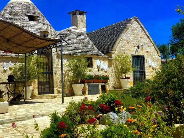 Ein Steinhaus mit einem spitzen Kegeldach, einem kleinen Turm und einem Garten voller bunter Blumen.