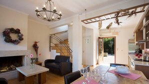 A modern living room with a fireplace, a dining table set with wine glasses, a staircase, and a kitchen area. - Aeriko-Ammos Beachfront Villa with Stunning View and Private Pool (LEFKADA)