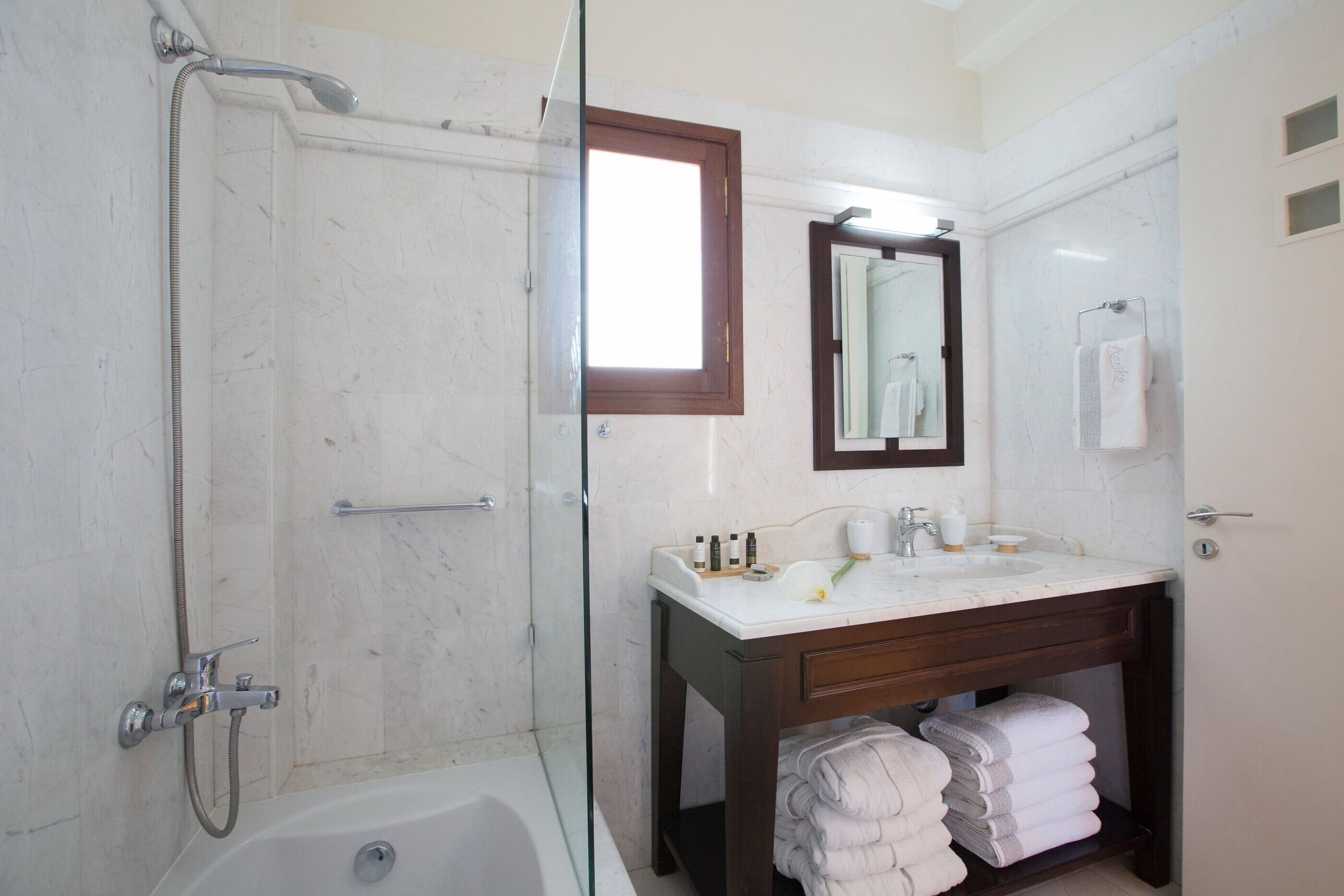 Un baño con ducha envuelta en vidrio, un lavamanos con artículos de aseo y un espejo encima.