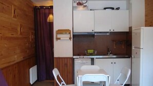 Une cuisine de taille réduite avec des meubles blancs, une petite table à manger et deux chaises.