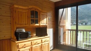 Une cabane en bois comprenant un coin cuisine, une table à manger et une grande fenêtre donnant sur un paysage verdoyant.