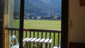 Une chambre avec un balcon donnant sur un champ verdoyant et des montagnes.