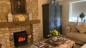 A cozy living room with a stone fireplace, a dark wooden cabinet, and a comfortable sofa. - Stunning Interior Designed 2 bedroom House in the center of Chipping Campden (Chipping Campden)
