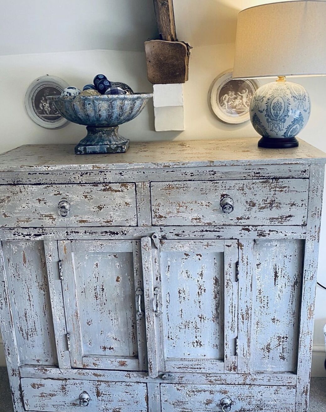A rustic, distressed wooden cabinet with multiple drawers and a decorative bowl on top.
