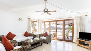 A spacious living room with wicker furniture, a ceiling fan, and a large TV on a stand. -  EXCELLENT TWO BEDROOMED  HOLIDAY HOME WITH STUNNING VIEWS AND PRIVATE POOL  (Amarilla Golf)