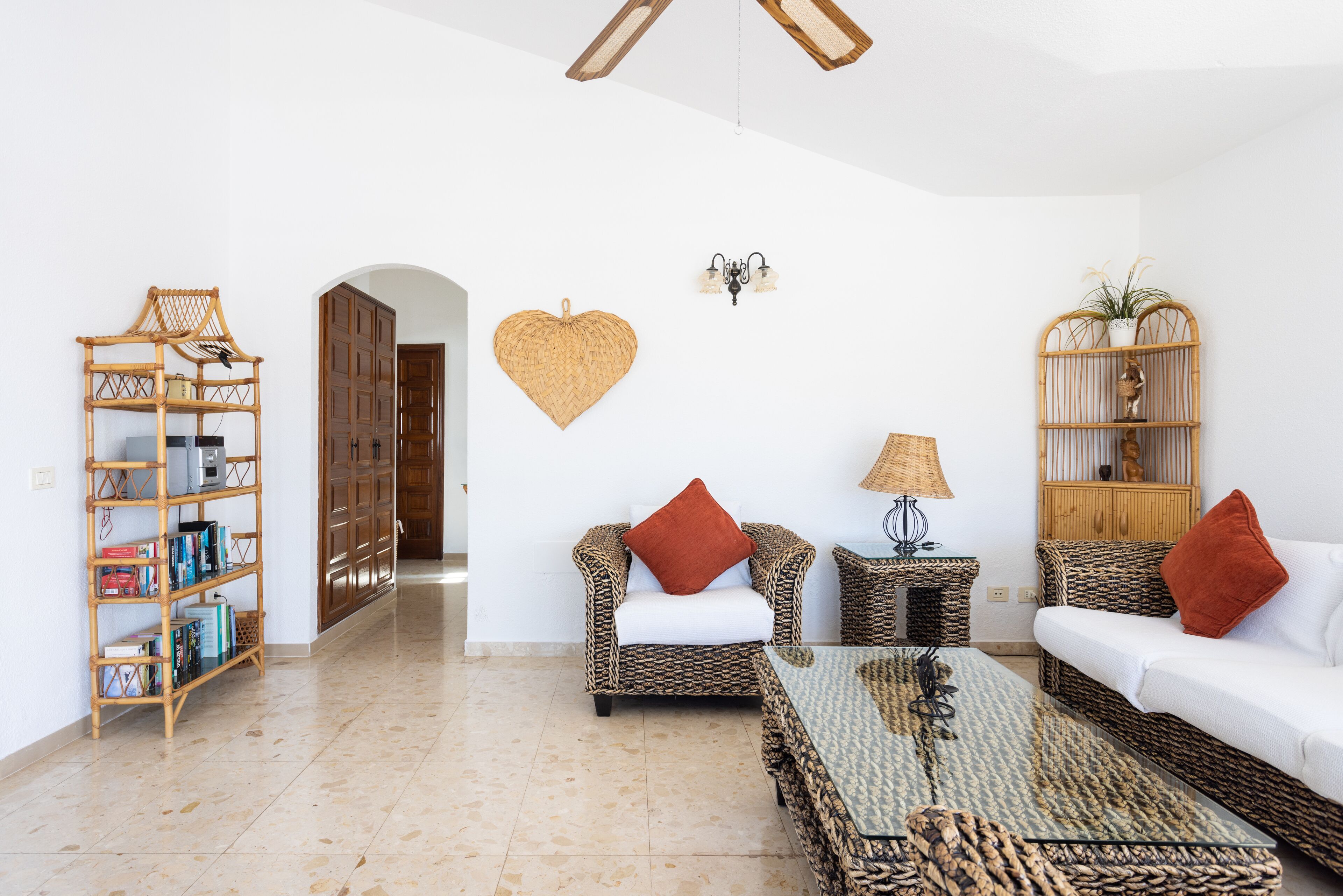 A spacious living room with a sofa, armchair, and a coffee table. There is a bookshelf and a decorative wall hanging.