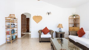 A spacious living room with a sofa, armchair, and a coffee table. There is a bookshelf and a decorative wall hanging. -  EXCELLENT TWO BEDROOMED  HOLIDAY HOME WITH STUNNING VIEWS AND PRIVATE POOL  (Amarilla Golf)