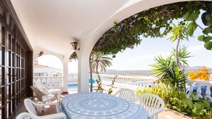 A covered outdoor seating area with a patterned tablecloth, white chairs, and a view of the sea. -  EXCELLENT TWO BEDROOMED  HOLIDAY HOME WITH STUNNING VIEWS AND PRIVATE POOL  (Amarilla Golf)