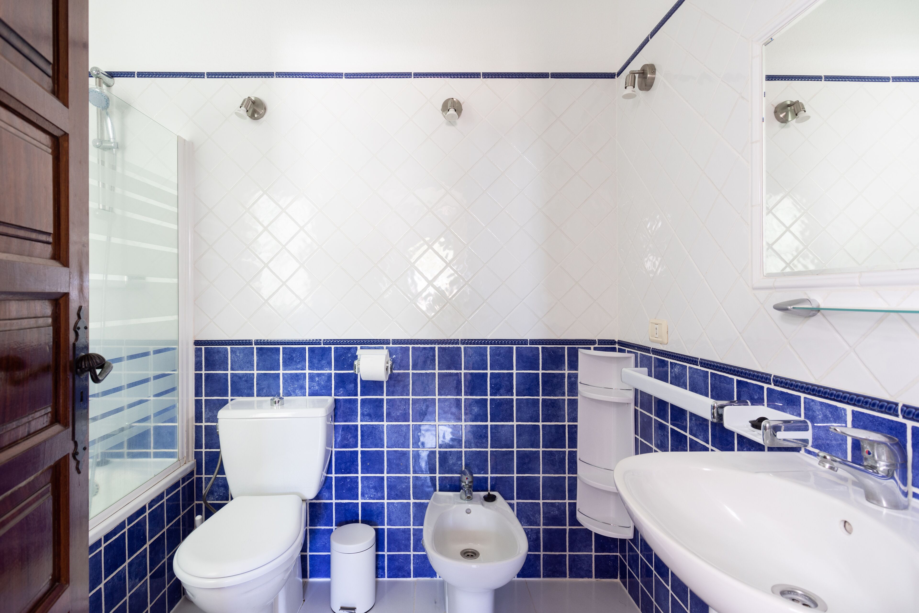 Un baño con inodoro, bidé y lavamanos, con azulejos azules y blancos.