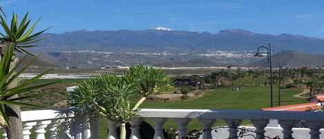 A balcony with a view of a golf course, mountains, and a clear sky.