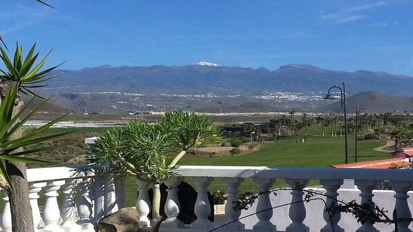 Un balcon offrant une vue sur un terrain de golf, des montagnes et un ciel dégagé.