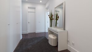 A hallway with white walls, a dark carpet, a white bench, and a mirror with flowers. - House Sweet Home - Lisbon Center (Lisboa)