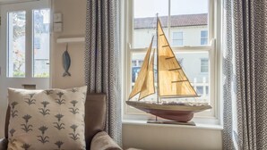 A cozy room with a window, a sailboat model, and patterned curtains. - Burnham Cottage, Wells-next-the-Sea, Norfolk (Wells-next-the-Sea)