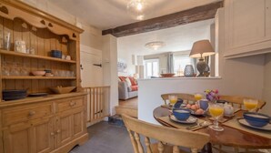 A kitchen with wooden cabinetry, a dining table set for breakfast, and a view into the living area. - Burnham Cottage, Wells-next-the-Sea, Norfolk (Wells-next-the-Sea)