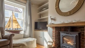 A cozy living room with a fireplace, a television, and a sailboat decoration. - Burnham Cottage, Wells-next-the-Sea, Norfolk (Wells-next-the-Sea)