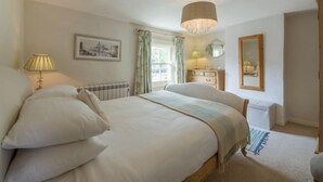 A bedroom with a large bed, a bedside table, a lamp, a mirror, and a window with curtains. - Burnham Cottage, Wells-next-the-Sea, Norfolk (Wells-next-the-Sea)