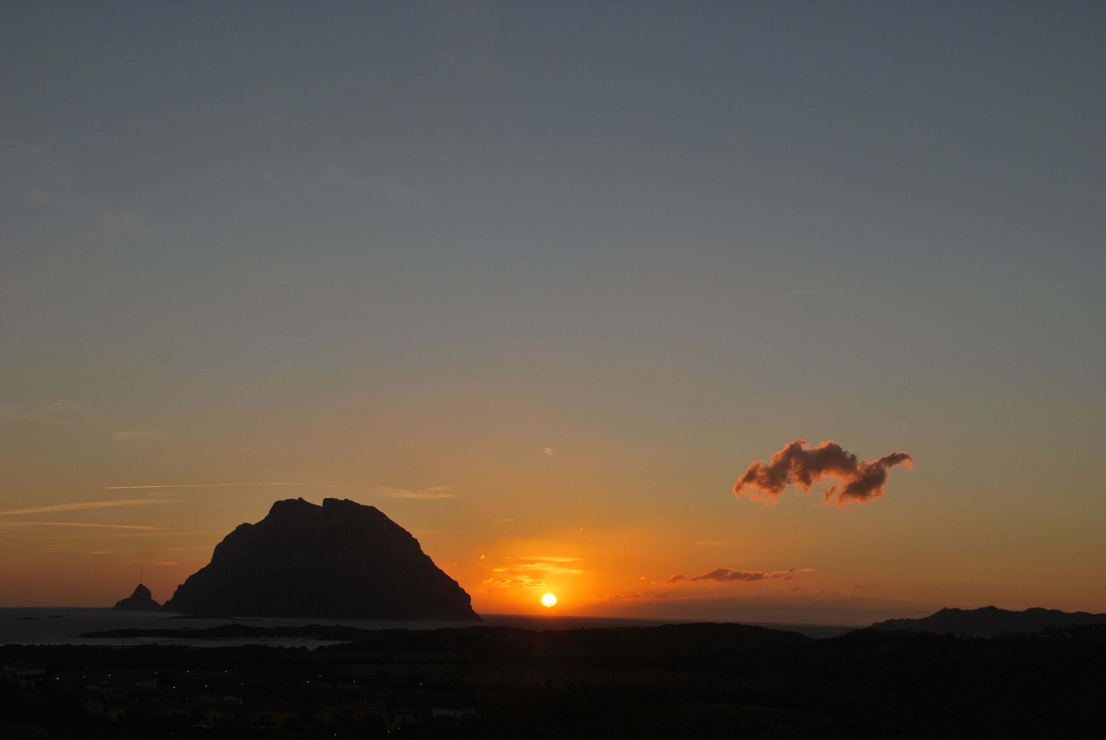 A sunset over a mountainous landscape with a prominent peak and a body of water in the foreground.