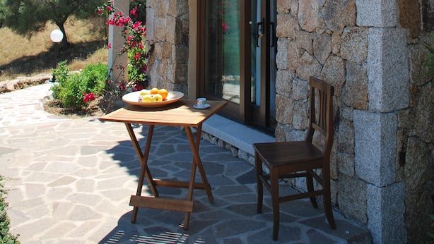A stone building with a balcony, a table with a chair, and a window.