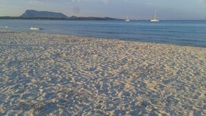 A sandy beach with boats in the water and mountains in the background.