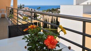 Un balcone con vista sul mare, un tavolo bianco e una pianta in vaso con fiori.