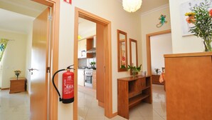 Un corridoio d'hotel con porte in legno, un estintore, una zona cucina e uno specchio al muro.