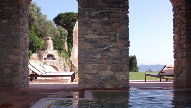 A stone archway leading to a pool area with a stone fireplace and lounge chairs.