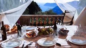 A dining table set up in a tent with a view of mountains and the sea.