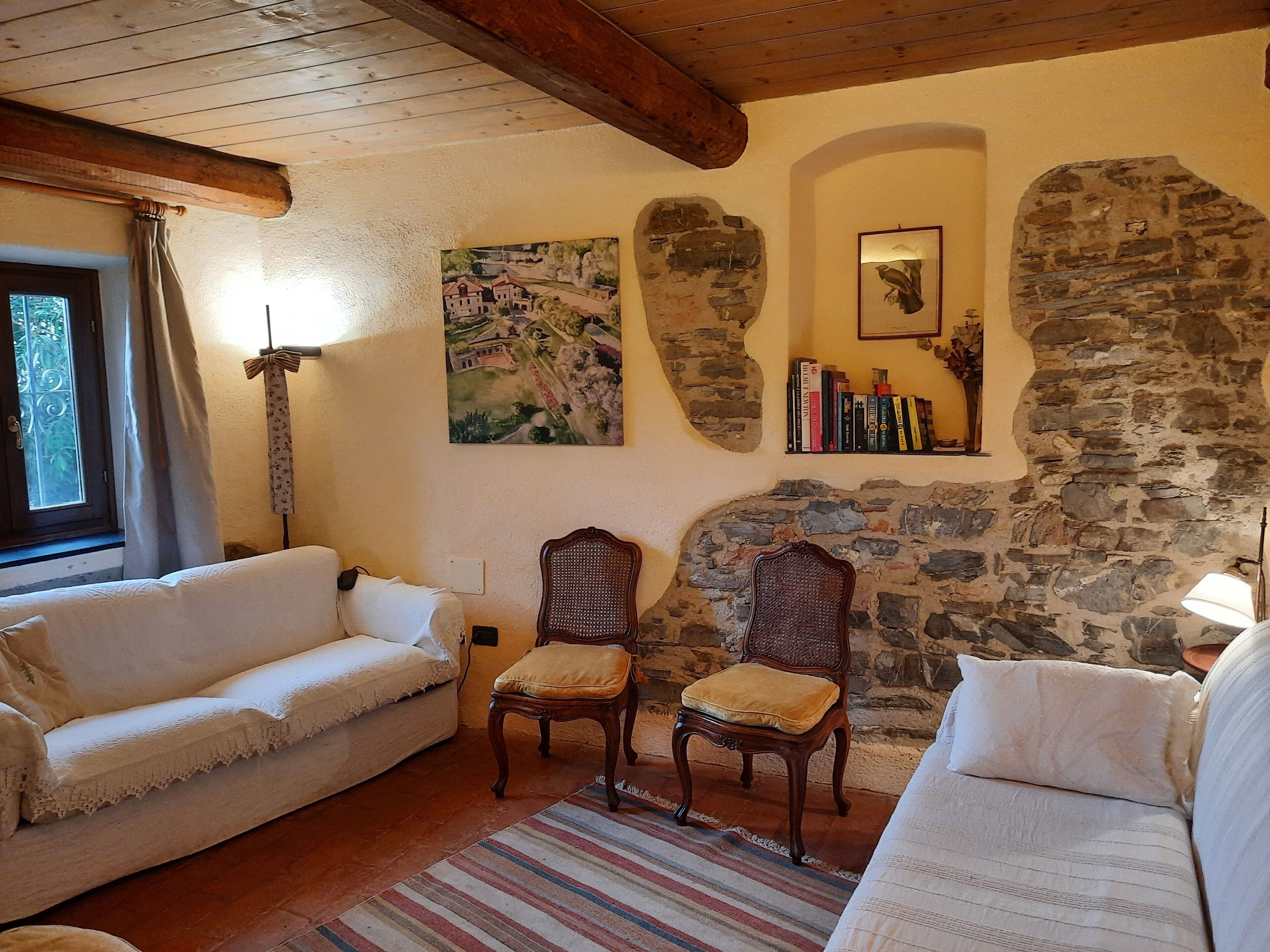 A cozy living room with a stone wall, a white sofa, a wooden chair, and a bookshelf.
