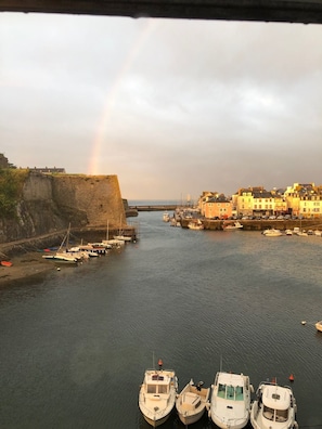 A harbor with boats docked, a rainbow in the distance, and buildings along the shore.